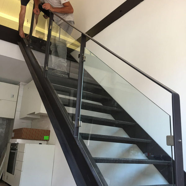 Imagen que muestra unas escaleras con baranda en aluminio y acristalada en la que incluye a dos personas trabajando en ella y unos muebles blancos en la planta baja.