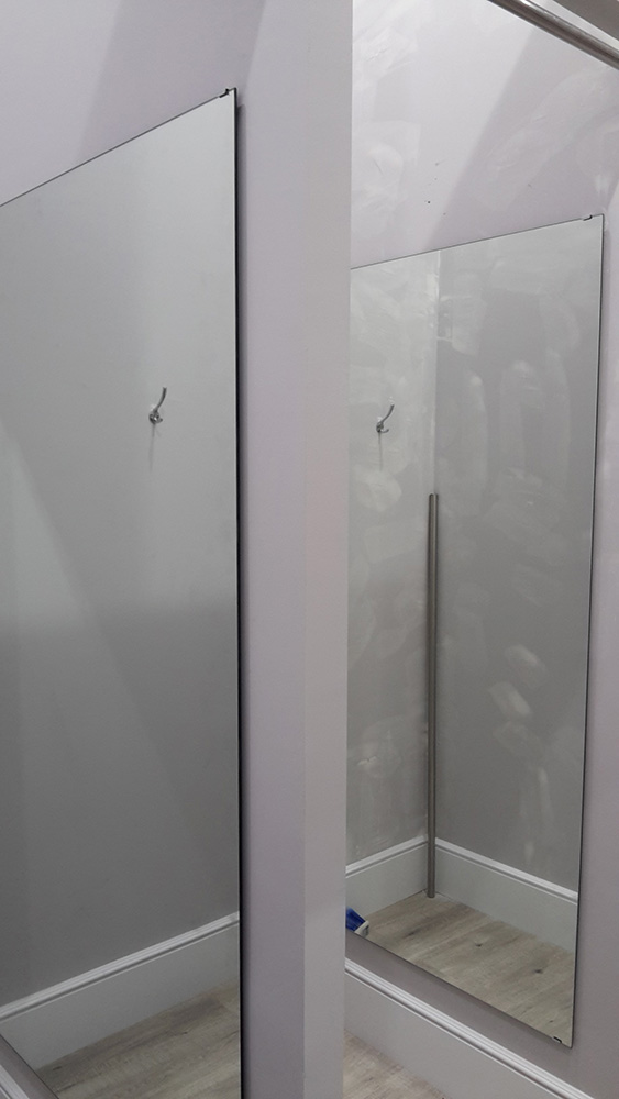 Imagen con detalle de un espejo colgado en la pared en la que se refleja un colgador y una barra de aluminio.
